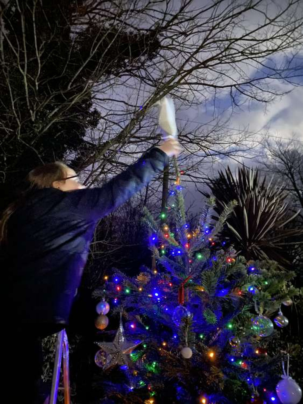 The star being put on the top of the tree.