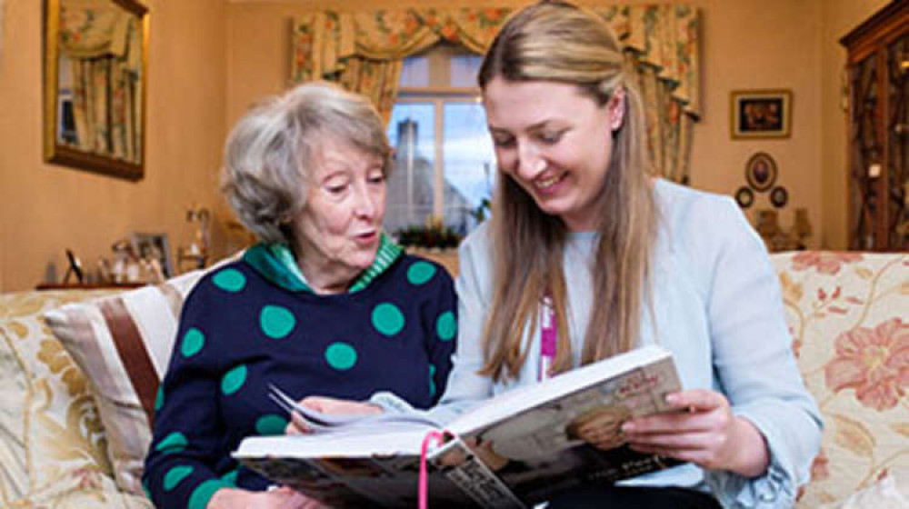 A Home Instead CAREGiver reading a book with a client (Image: Home Instead)