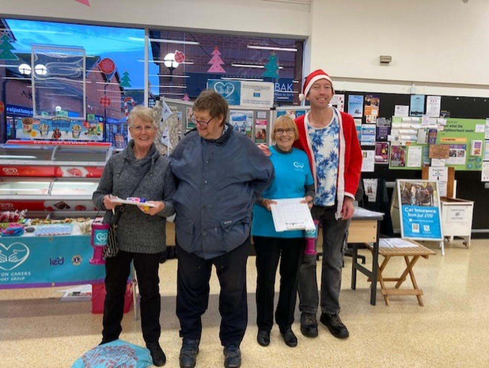 The winning hamper ticket being drawn by a member of the co-op staff supporting him on the left is Barbara East on the right is Valerie Lloyd, both volunteers with Honiton Carers (Credit: Winnie Cameron)