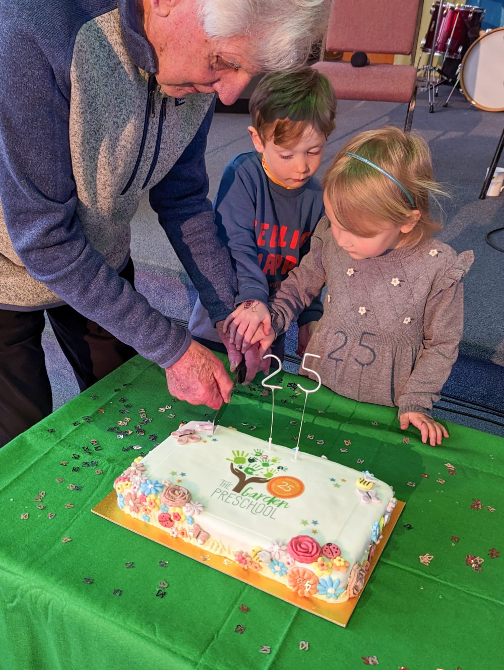 Long standing committee member Ingram Bright cuts cake with pre school children 