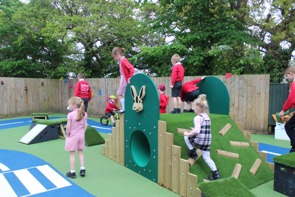 The play area includes bespoke wooden play equipment with a tunnel