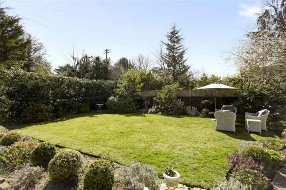 A view of the lawn from the others side showing garden chairs under a parasol near the garden wall