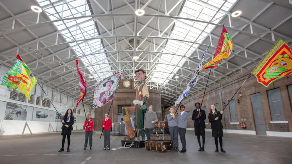 Supporters have been celebrating news of a successful granbt application. Pictured are former dock worker Les Morgan (centre) and children from the Gateway Learning Academy schools (waving flags representing the Windrush generation), alongside Tilbury port's 16ft docker puppet, celebrate the Tilbury Riverside Station grant in the building that will be transformed into a creative community hub.