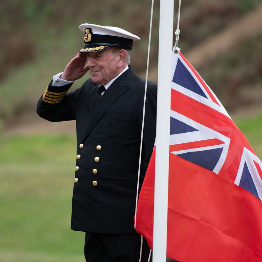 Captain Bob Strick salutes the raising of the Red Ensign.