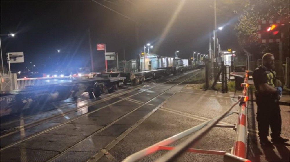 BTP officer at crossing while freight train, made up of many empty wagons, was stopped at station BTP officer at crossing while freight train, made up of many empty wagons, was stopped at station